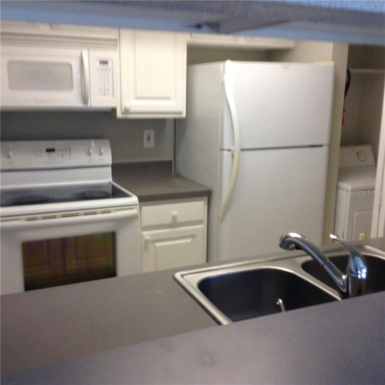 A kitchen features white appliances, white cabinets, and a double-basin sink with a dark countertop — 3716 IDLEBROOK CIRCLE UNIT 110, CASSELBERRY, FL