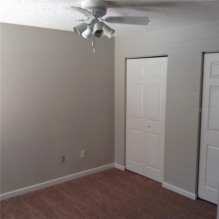 A bedroom with beige walls, brown carpet, a ceiling fan, and two white closet doors — 3716 IDLEBROOK CIRCLE UNIT 110, CASSELBERRY, FL