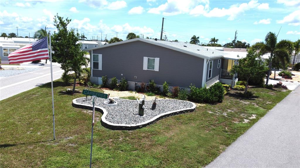 An exterior view of a gray manufactured home with a landscaped rock garden and flag — 602 CAREFREE, VENICE, FL