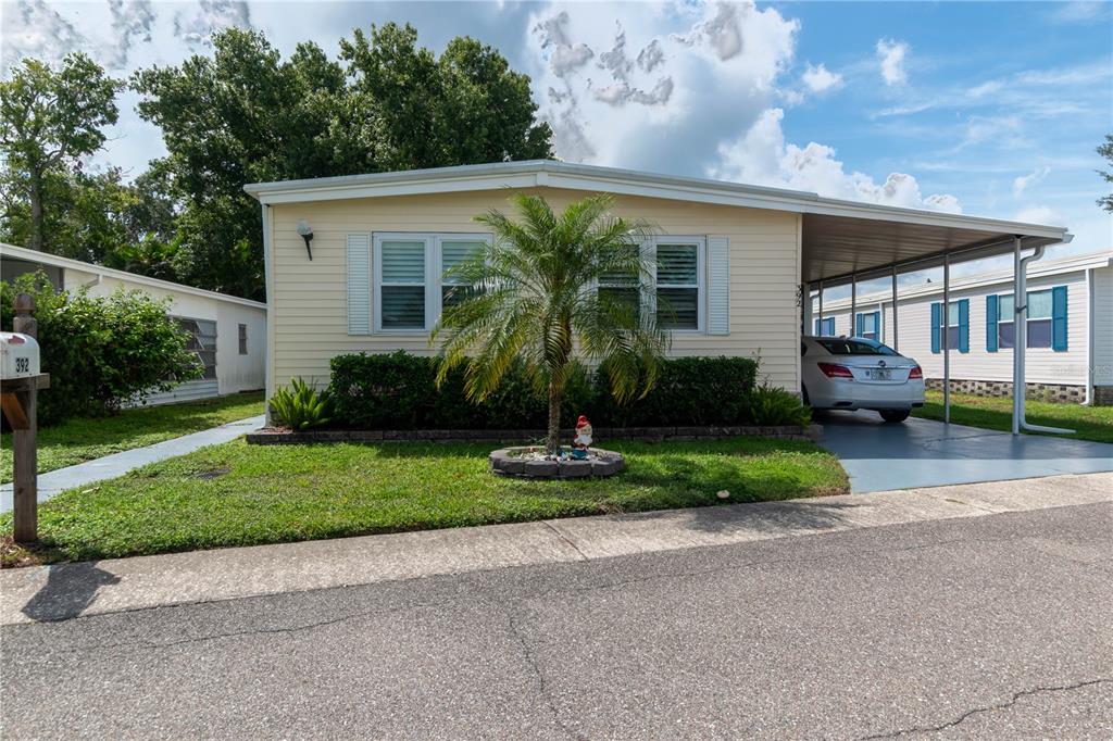 A light yellow mobile home features a palm tree in the front yard and a carport — 392 COBIA WAY, OLDSMAR, FL