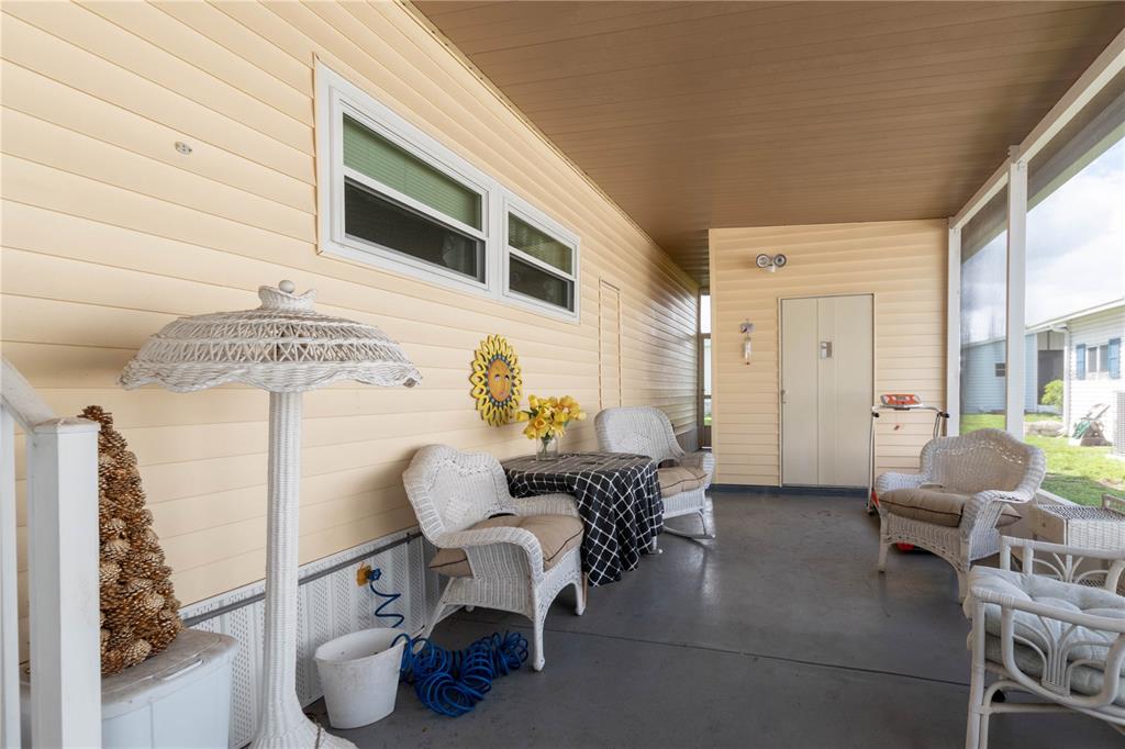 A covered porch features light yellow siding, white wicker furniture, and a concrete floor — 392 COBIA WAY, OLDSMAR, FL
