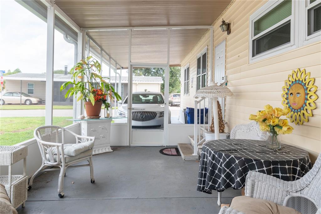 A screened-in porch features a concrete floor, white wicker furniture, and a yellow sun wall decoration — 392 COBIA WAY, OLDSMAR, FL