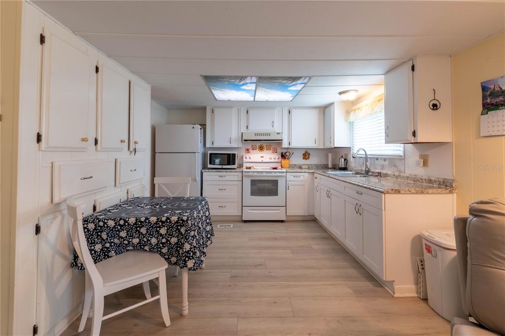 A kitchen features white cabinets, a dining table with a patterned cloth, and light flooring — 392 COBIA WAY, OLDSMAR, FL