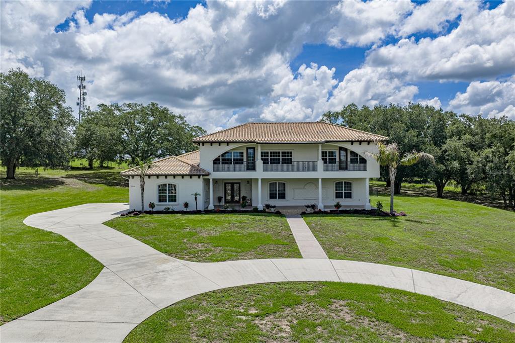 A two-story stucco house with a tiled roof, balcony, and a curved concrete driveway — 37624 SKY RIDGE CIRCLE, DADE CITY, FL