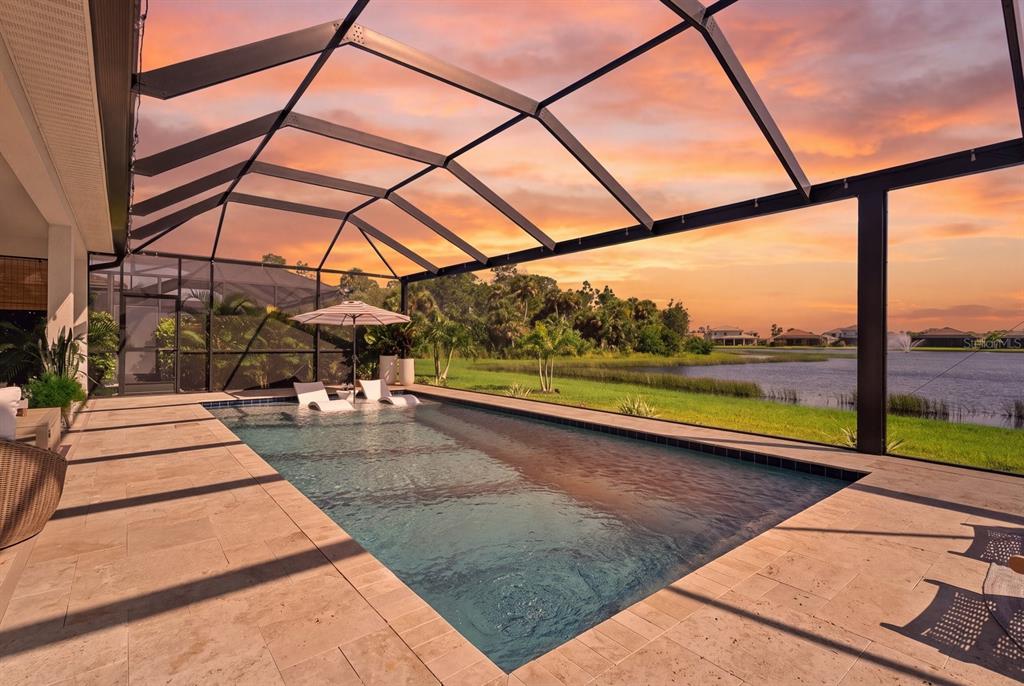 A screened-in patio features a swimming pool with a tanning ledge and lake views — 12801 MORNING MIST PLACE, VENICE, FL