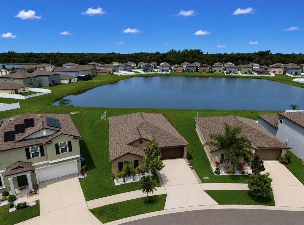 An aerial view shows three suburban houses with driveways facing a large retention pond — 12741 TRIPOLI AVENUE, RIVERVIEW, FL