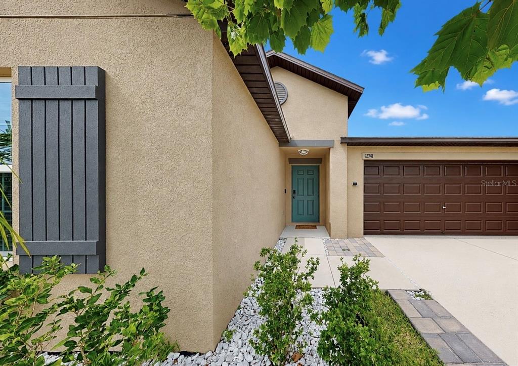 A tan stucco house exterior features a teal front door and a brown garage door — 12741 TRIPOLI AVENUE, RIVERVIEW, FL