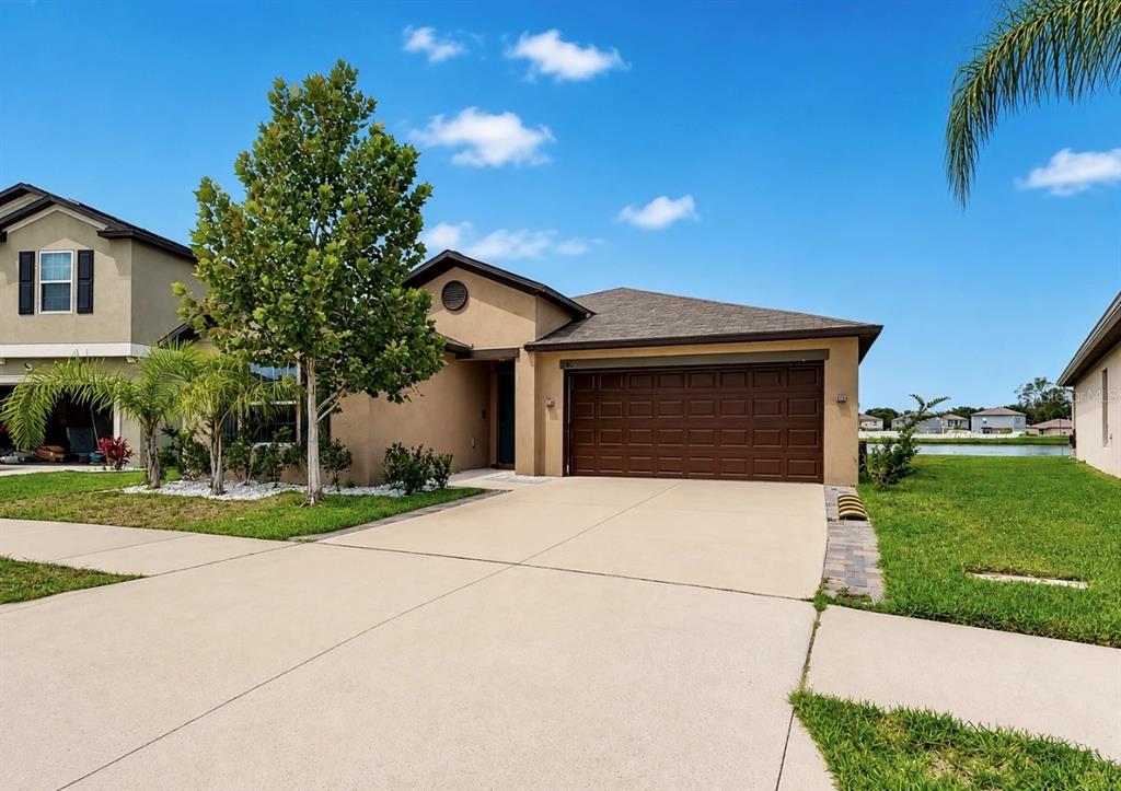 A tan single-story house features a brown garage door, a concrete driveway, and a front lawn — 12741 TRIPOLI AVENUE, RIVERVIEW, FL