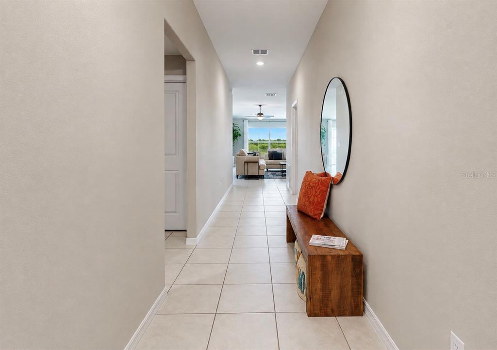 A tiled hallway leads to a living room with a wooden bench and oval mirror — 12741 TRIPOLI AVENUE, RIVERVIEW, FL