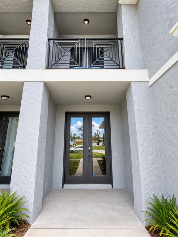 A ground-level entryway features double glass doors beneath a second-story balcony with metal railings — 328 DUNDEE DRIVE, KISSIMMEE, FL