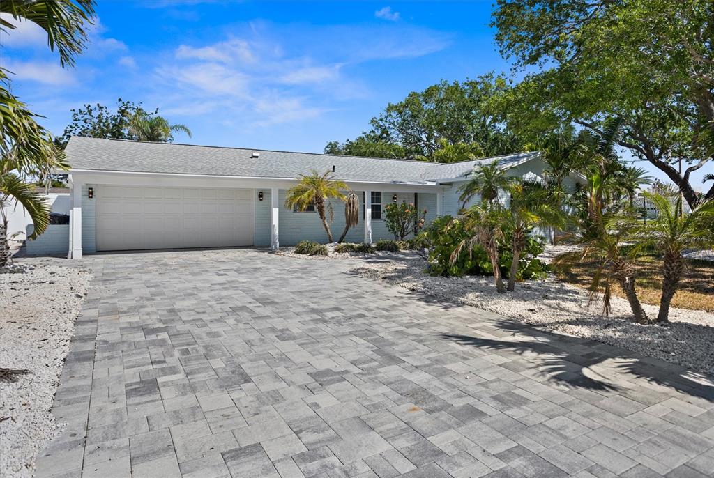 A light blue single-story house features a paver driveway, a two-car garage, and palm trees — 10001 S YACHT CLUB DRIVE, TREASURE ISLAND, FL
