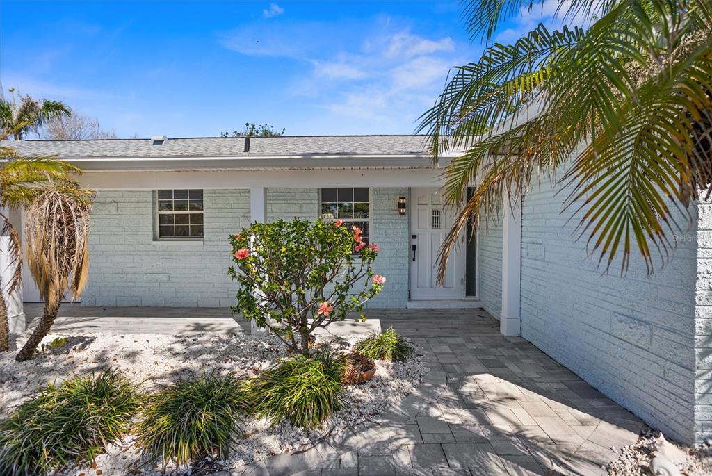 A light blue brick house exterior features a covered porch, a front door, and landscaping — 10001 S YACHT CLUB DRIVE, TREASURE ISLAND, FL
