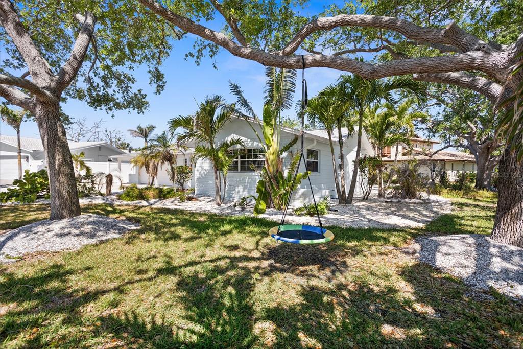 A white house with a saucer swing hanging from a large tree in the front yard — 10001 S YACHT CLUB DRIVE, TREASURE ISLAND, FL