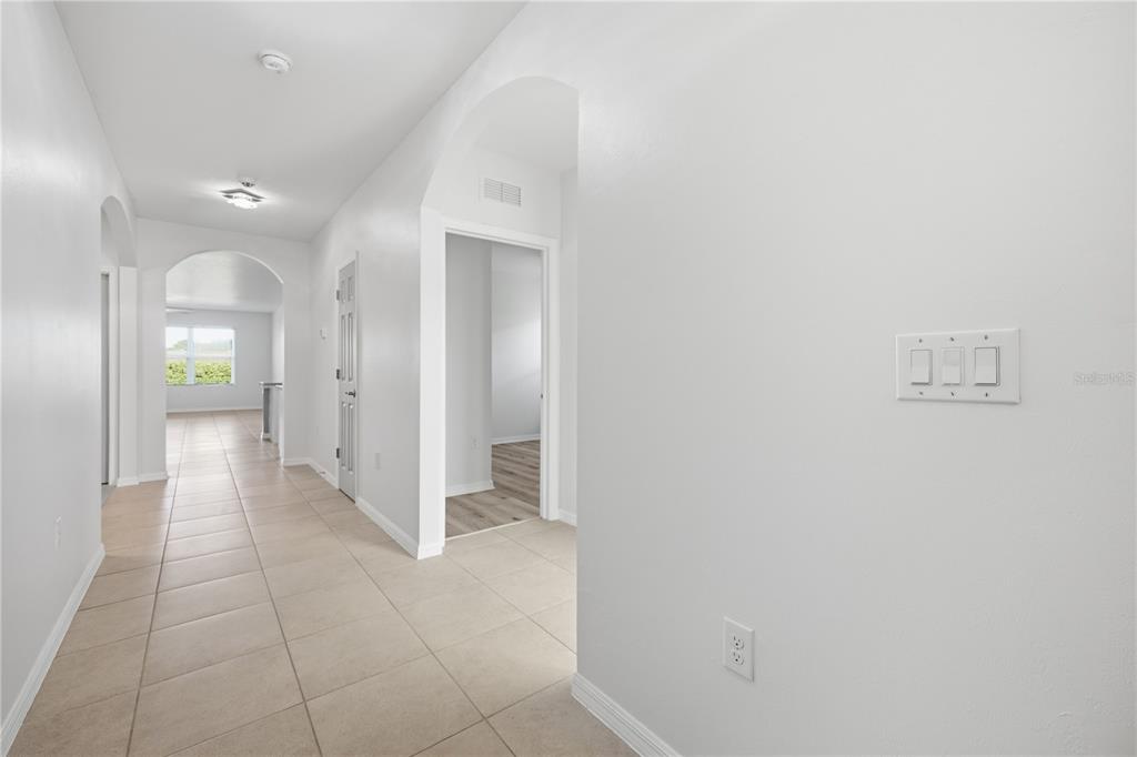 A hallway with beige tile flooring leads to an arched entryway and interior rooms — 10288 SILVER POND LANE, LEHIGH ACRES, FL