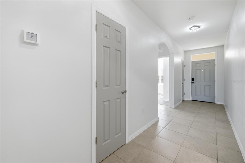 A hallway with light tile flooring leads to a gray front door and an arched entryway — 10288 SILVER POND LANE, LEHIGH ACRES, FL