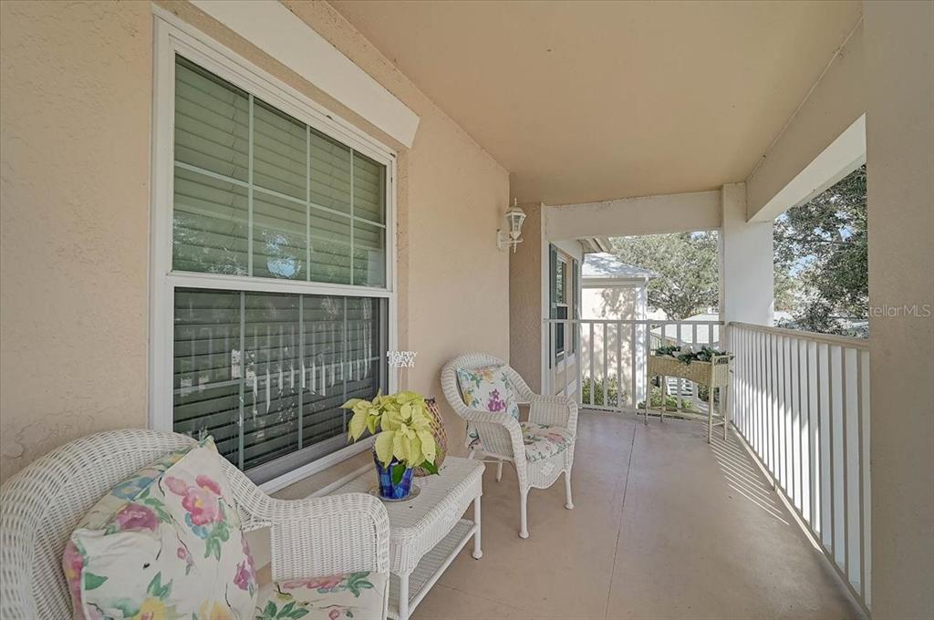 A covered balcony features white wicker furniture, a small table with a plant, and railings — 4219 CADDIE DRIVE E UNIT 204, BRADENTON, FL