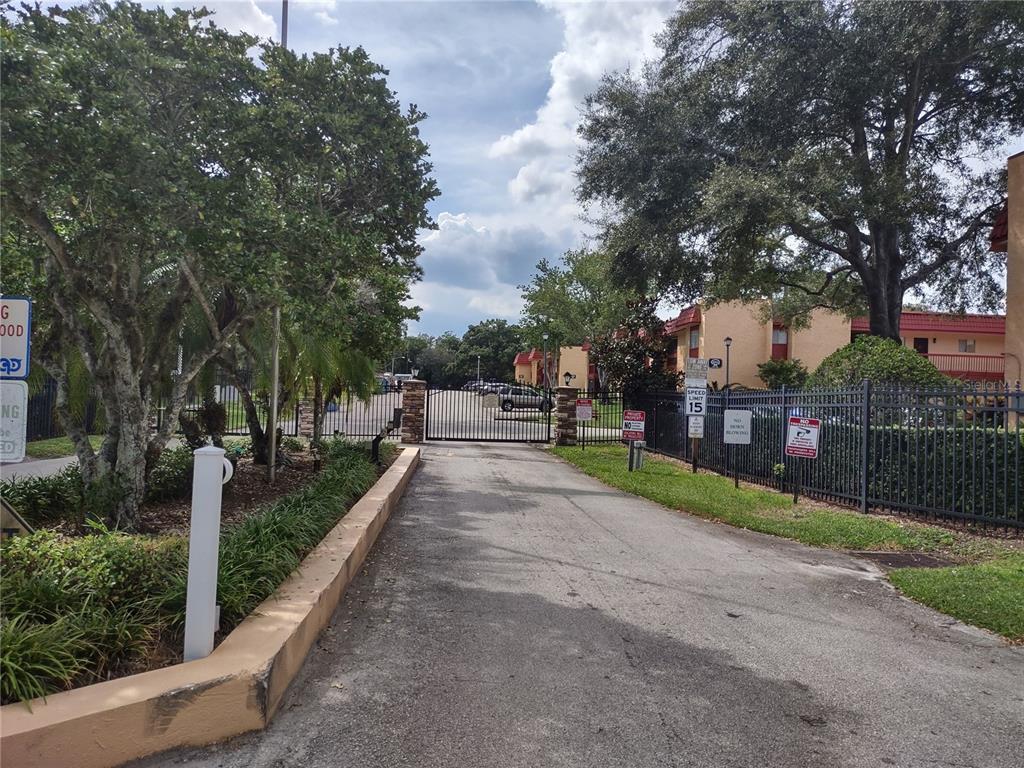 A paved driveway leads to a gated entrance of an apartment complex with mature trees — 2860 N POWERS DRIVE UNIT 8, ORLANDO, FL
