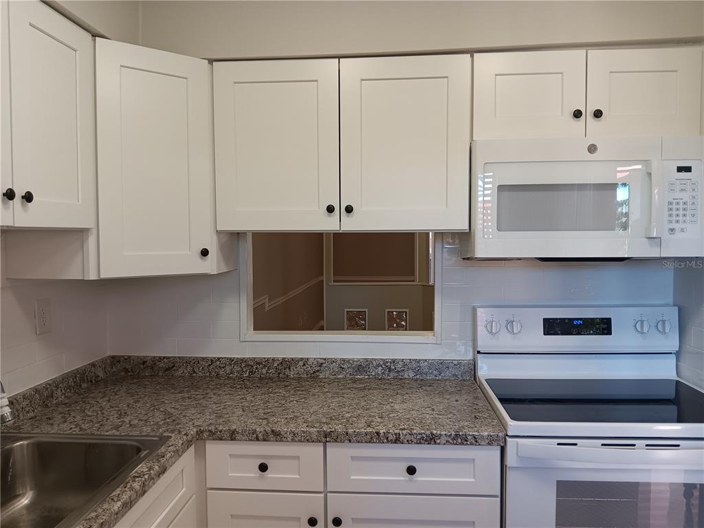 A kitchen features white cabinets, granite countertops, a white microwave, and a white stove — 2860 N POWERS DRIVE UNIT 8, ORLANDO, FL