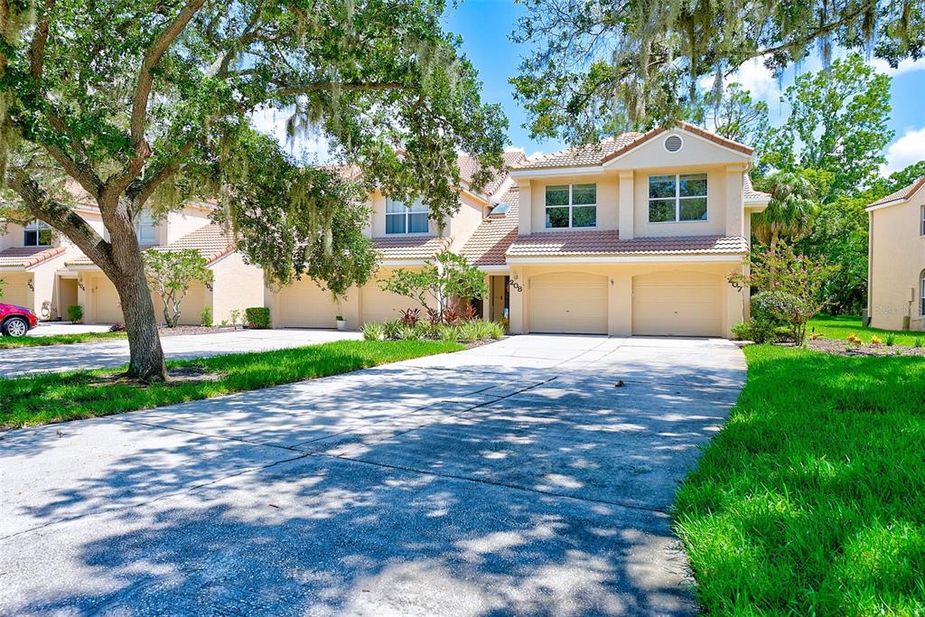 A two-story townhouse with a beige exterior, two garage doors, and a concrete driveway — 208 CLAYS TRAIL UNIT 208, OLDSMAR, FL