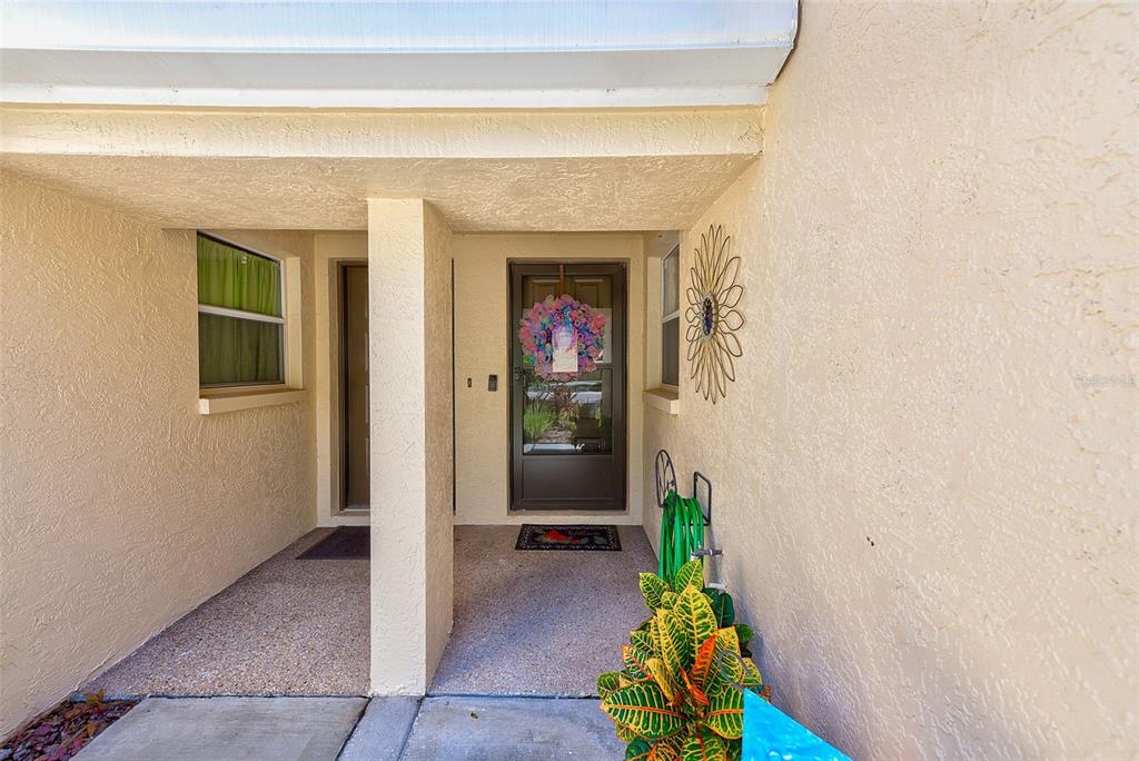 A covered entryway features a front door with a wreath, a side window, and stucco walls — 208 CLAYS TRAIL UNIT 208, OLDSMAR, FL