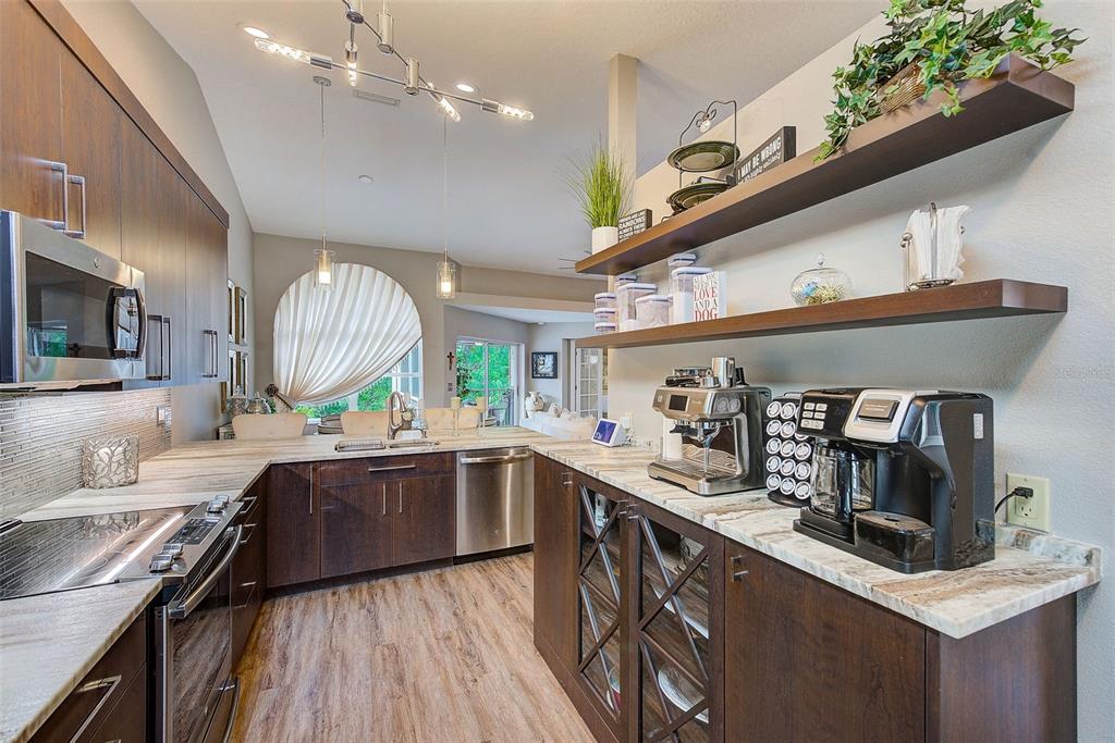 A modern kitchen features dark wood cabinets, stone countertops, open shelving, and stainless steel appliances — 208 CLAYS TRAIL UNIT 208, OLDSMAR, FL