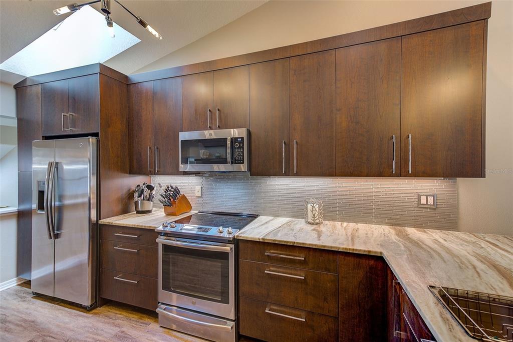 A kitchen features dark wood cabinets, stainless steel appliances, and a patterned stone countertop — 208 CLAYS TRAIL UNIT 208, OLDSMAR, FL