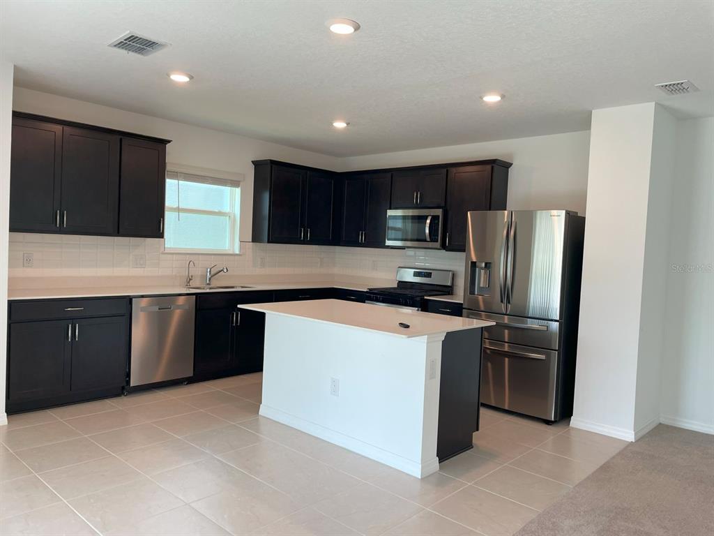 A kitchen features dark wood cabinets, stainless steel appliances, a white island, and tile flooring — 3943 ALMOND BROOK BOULEVARD, LAND O LAKES, FL