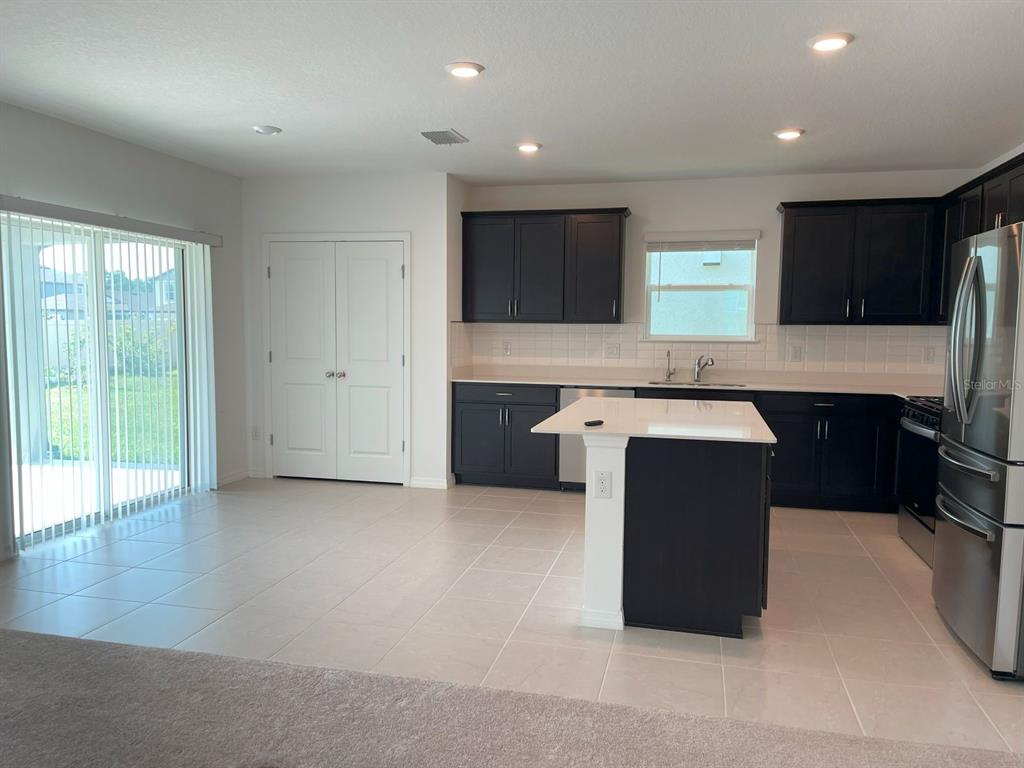 A kitchen with dark cabinets, a white island, and tile flooring next to a sliding door — 3943 ALMOND BROOK BOULEVARD, LAND O LAKES, FL