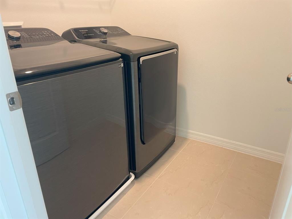 A laundry room features dark gray Samsung washer and dryer units on a tiled floor — 3943 ALMOND BROOK BOULEVARD, LAND O LAKES, FL
