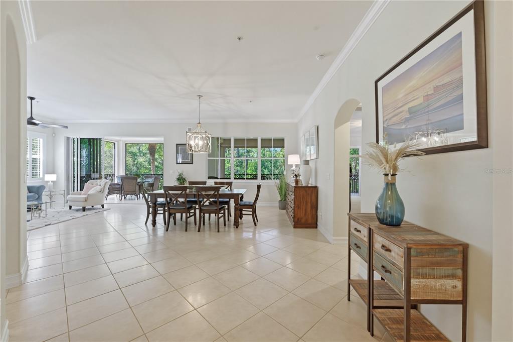 An open-concept dining and living area features tile flooring, a wooden table, and arched doorways — 2859 TIBURON BOULEVARD E UNIT 102, NAPLES, FL