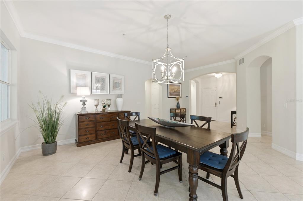 A dining room features a dark wood table with chairs, a matching sideboard, and chandelier — 2859 TIBURON BOULEVARD E UNIT 102, NAPLES, FL