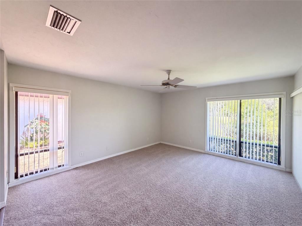 An empty room with beige carpet, a ceiling fan, and two large sliding glass doors — 109 TUXFORD DRIVE, HAINES CITY, FL