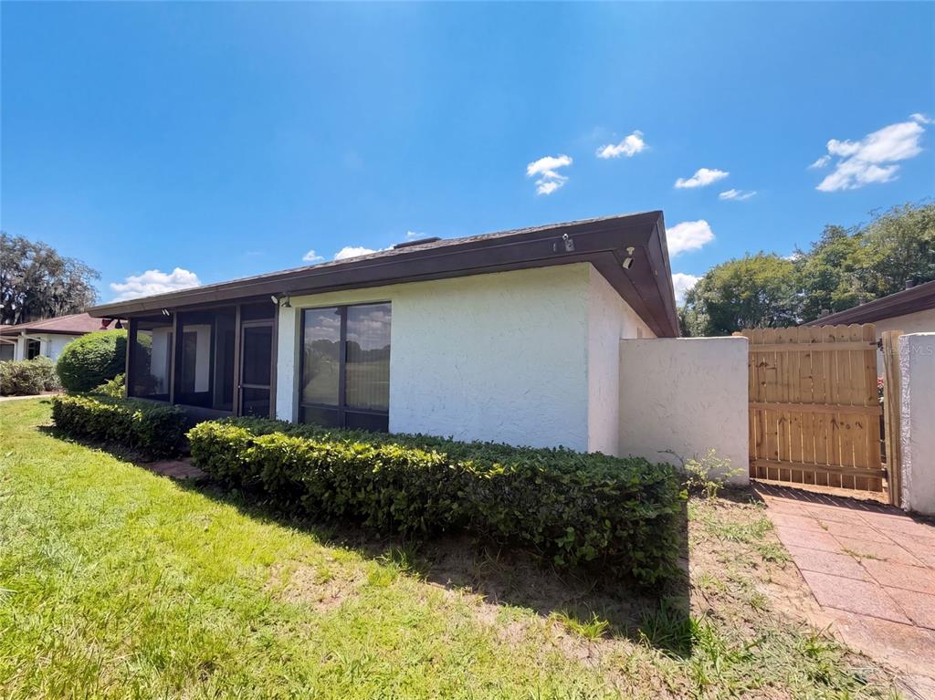 A white stucco house features a screened-in porch, dark trim, and a wooden privacy gate — 109 TUXFORD DRIVE, HAINES CITY, FL