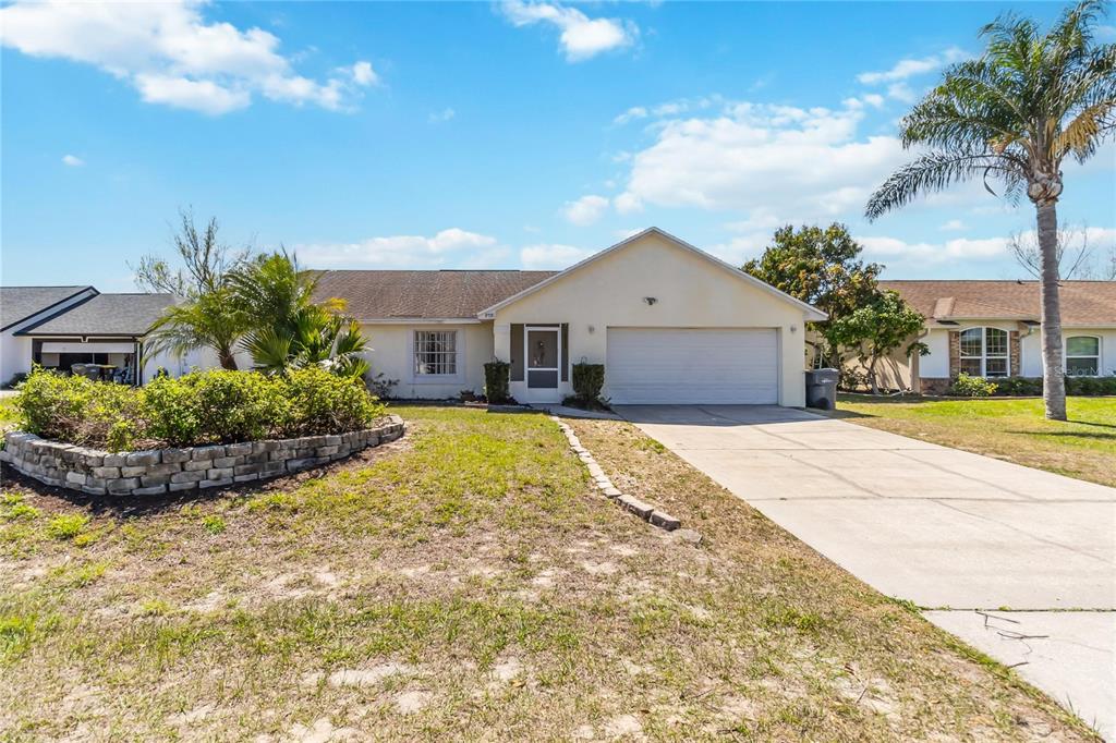 A single-story house with a beige exterior, a two-car garage, and a front yard garden — 959 LOMA BONITA DRIVE, DAVENPORT, FL