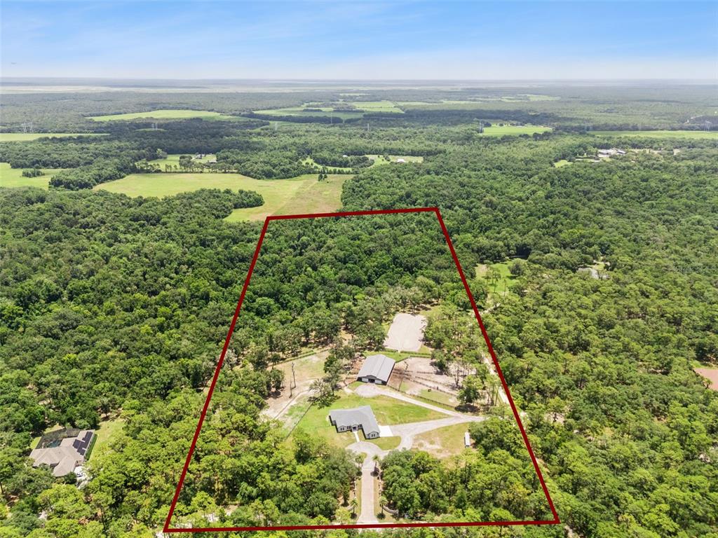 An aerial view shows a house, a large barn, and fenced pastures surrounded by trees — 2370 PINE MEADOWS PLACE, OVIEDO, FL