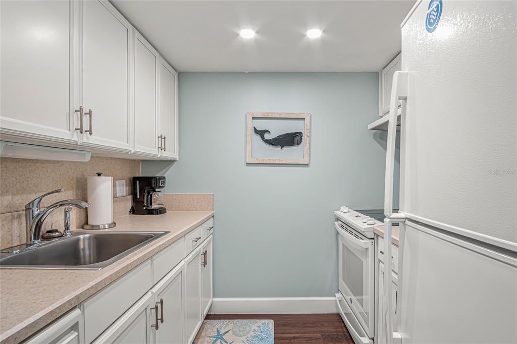 A galley kitchen features white cabinets, light countertops, a stainless steel sink, and white appliances — 2820 OCEAN SHORE BOULEVARD UNIT 26, ORMOND BEACH, FL