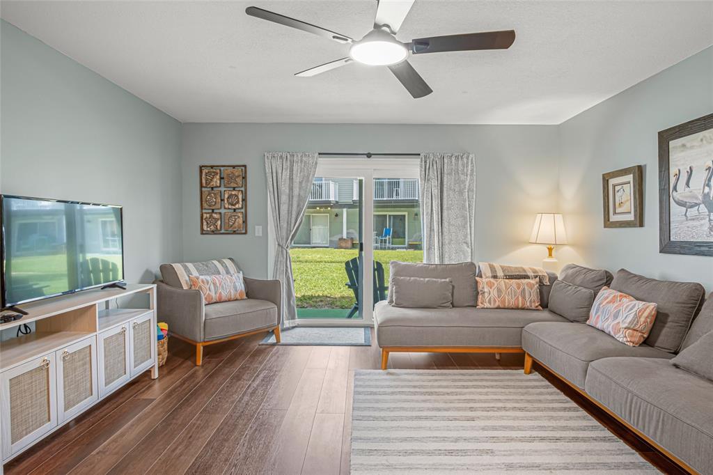 A living room features a gray sectional sofa, armchair, media console, and sliding glass doors — 2820 OCEAN SHORE BOULEVARD UNIT 26, ORMOND BEACH, FL