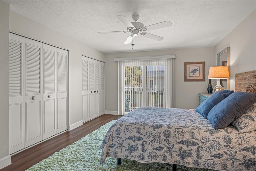 A bedroom features a bed with a patterned quilt, white louvered closets, and sliding glass doors — 2820 OCEAN SHORE BOULEVARD UNIT 26, ORMOND BEACH, FL