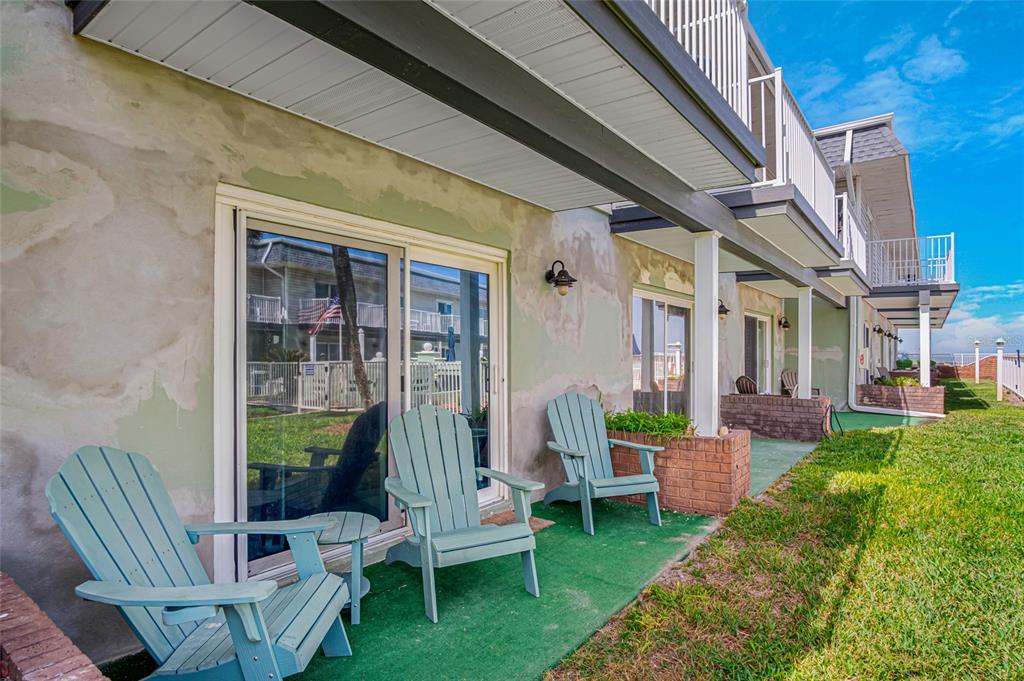 A ground-level patio with green carpeting and light blue Adirondack chairs sits outside sliding doors — 2820 OCEAN SHORE BOULEVARD UNIT 26, ORMOND BEACH, FL