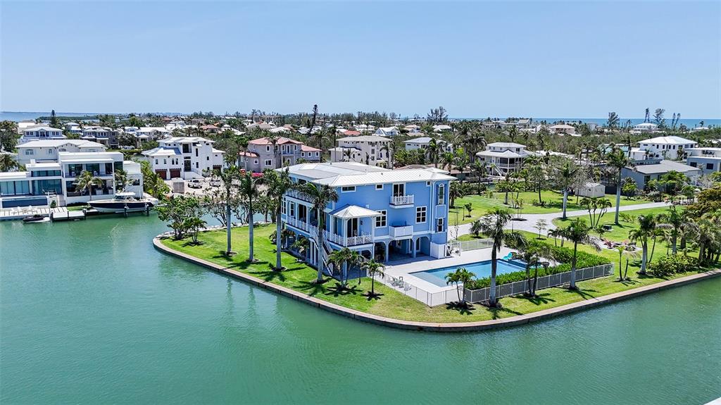 An aerial view shows a blue multi-story house with a pool on a waterfront lot — 630 DE NARVAEZ DRIVE, LONGBOAT KEY, FL
