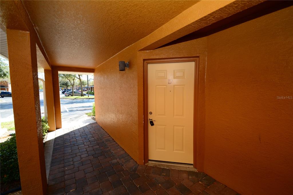 A beige front door is set into a covered walkway with orange walls and brick flooring — 4600 E MOODY BOULEVARD UNIT 8D, BUNNELL, FL