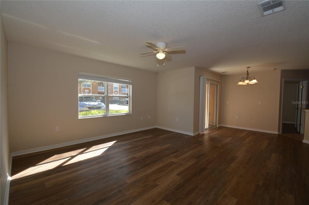 An empty living room features wood-look flooring, a ceiling fan, and a sliding glass door — 4600 E MOODY BOULEVARD UNIT 8D, BUNNELL, FL