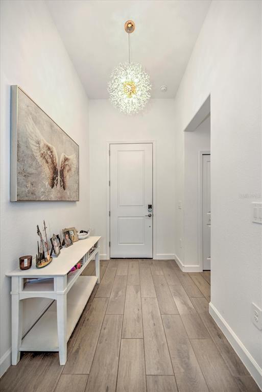 A bright entryway features a white console table, a modern chandelier, and wood-look tile flooring — 3254 WESTON MANOR DRIVE, ALVA, FL