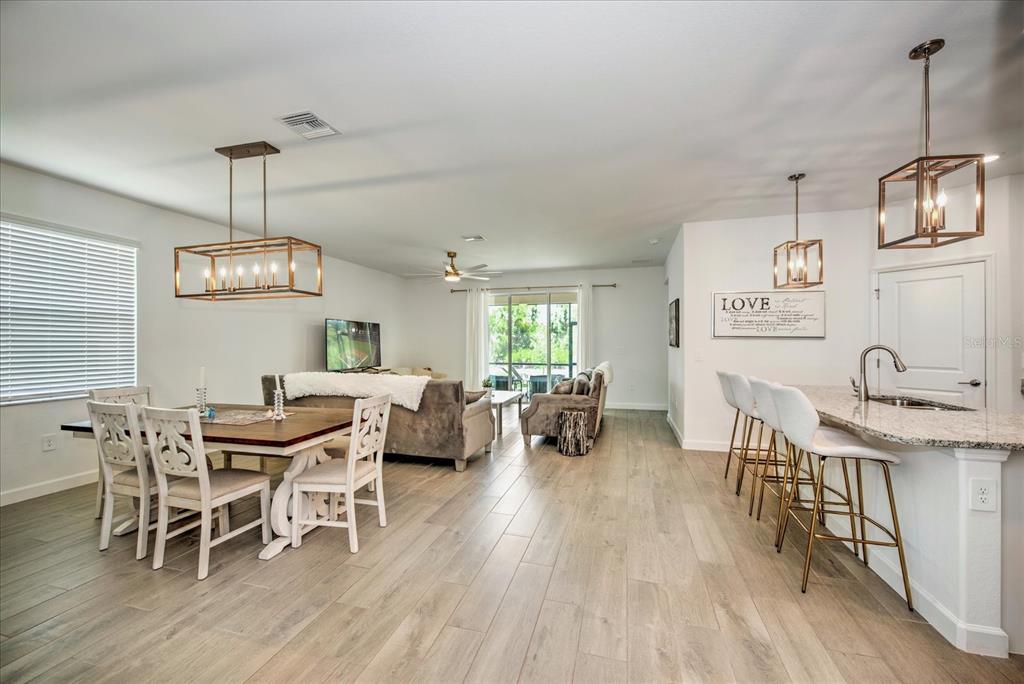 An open-concept living and dining area features light wood-look tile flooring and modern pendant lighting — 3254 WESTON MANOR DRIVE, ALVA, FL