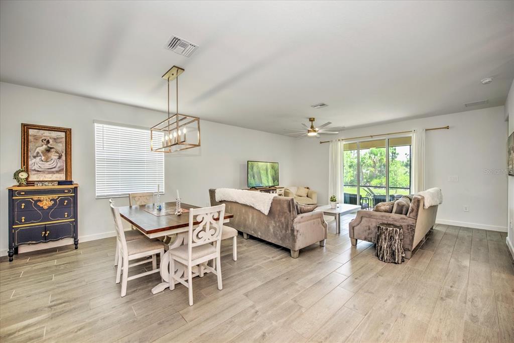 An open-concept living and dining area features wood-look tile flooring and a modern light fixture — 3254 WESTON MANOR DRIVE, ALVA, FL