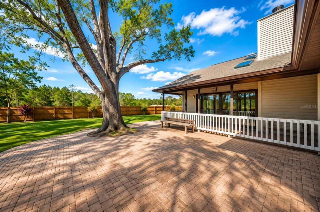 A large tree stands beside a brick patio and a house with a white railing — 9502 59TH AVENUE E, BRADENTON, FL