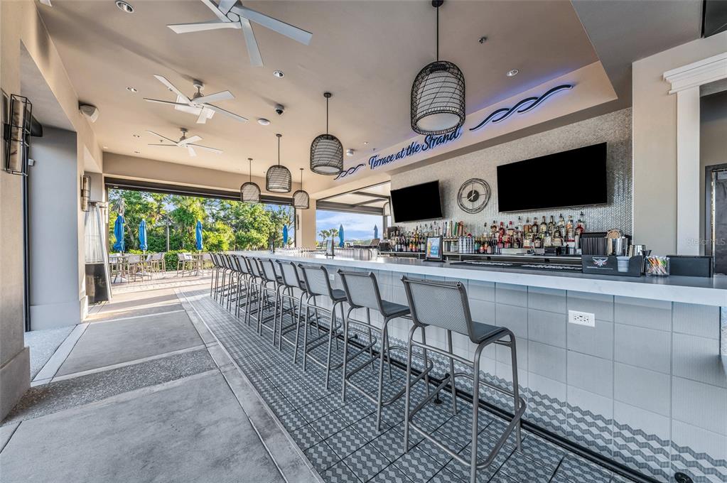 An outdoor bar features a long counter, numerous stools, pendant lighting, and ceiling fans — 8105 GRAND ESTUARY TRAIL UNIT 404, BRADENTON, FL