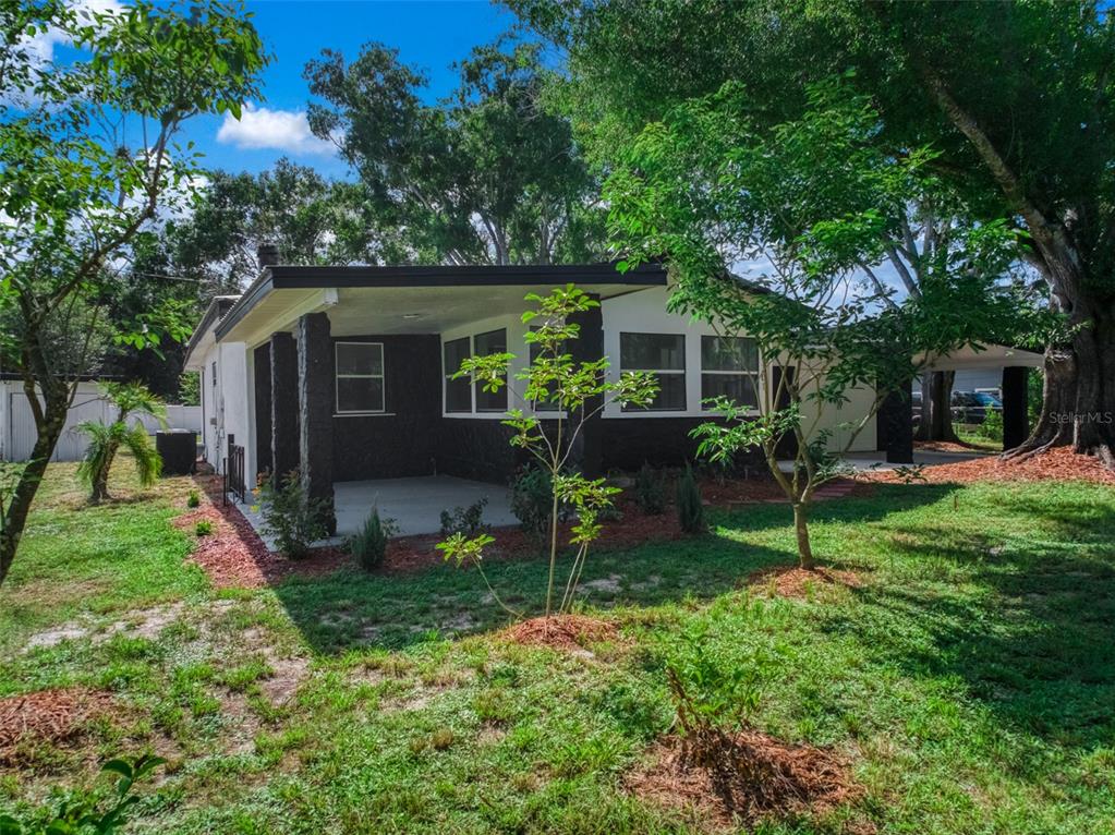 The exterior of a house features a covered patio, dark masonry walls, and surrounding trees — 201 BROOKS ROAD, FROSTPROOF, FL
