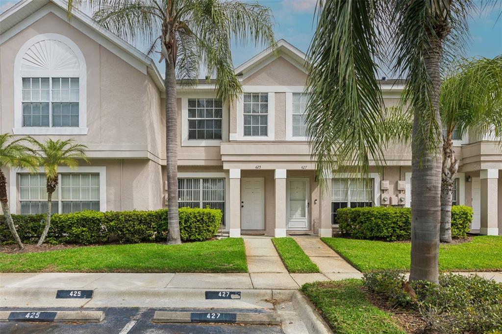 A two-story townhouse exterior with beige siding, palm trees, and designated parking spaces — 425 KENSINGTON LAKE CIRCLE, BRANDON, FL