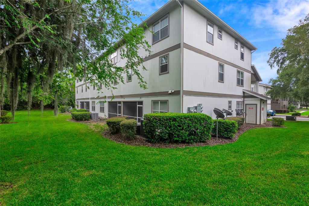A three-story apartment building with a white exterior, screened-in patios, and surrounding green lawn — 6519 W NEWBERRY ROAD UNIT A10, GAINESVILLE, FL